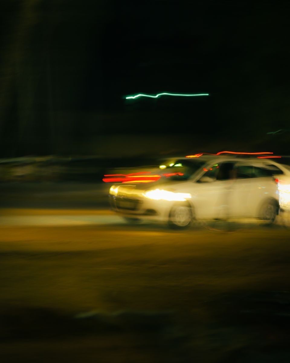 Blurred image of a fast-moving white car on a highway at night.